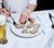 Woman eating oysters off of a white porcelain Dinner Plate using Black Satin Flatware.  Filled Pilsner Glass on the side.