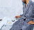 Man sitting in shower spa, lighting a candle wearing the Slate Blue Classic Bathrobe.  Towel and soap dish on ledge.