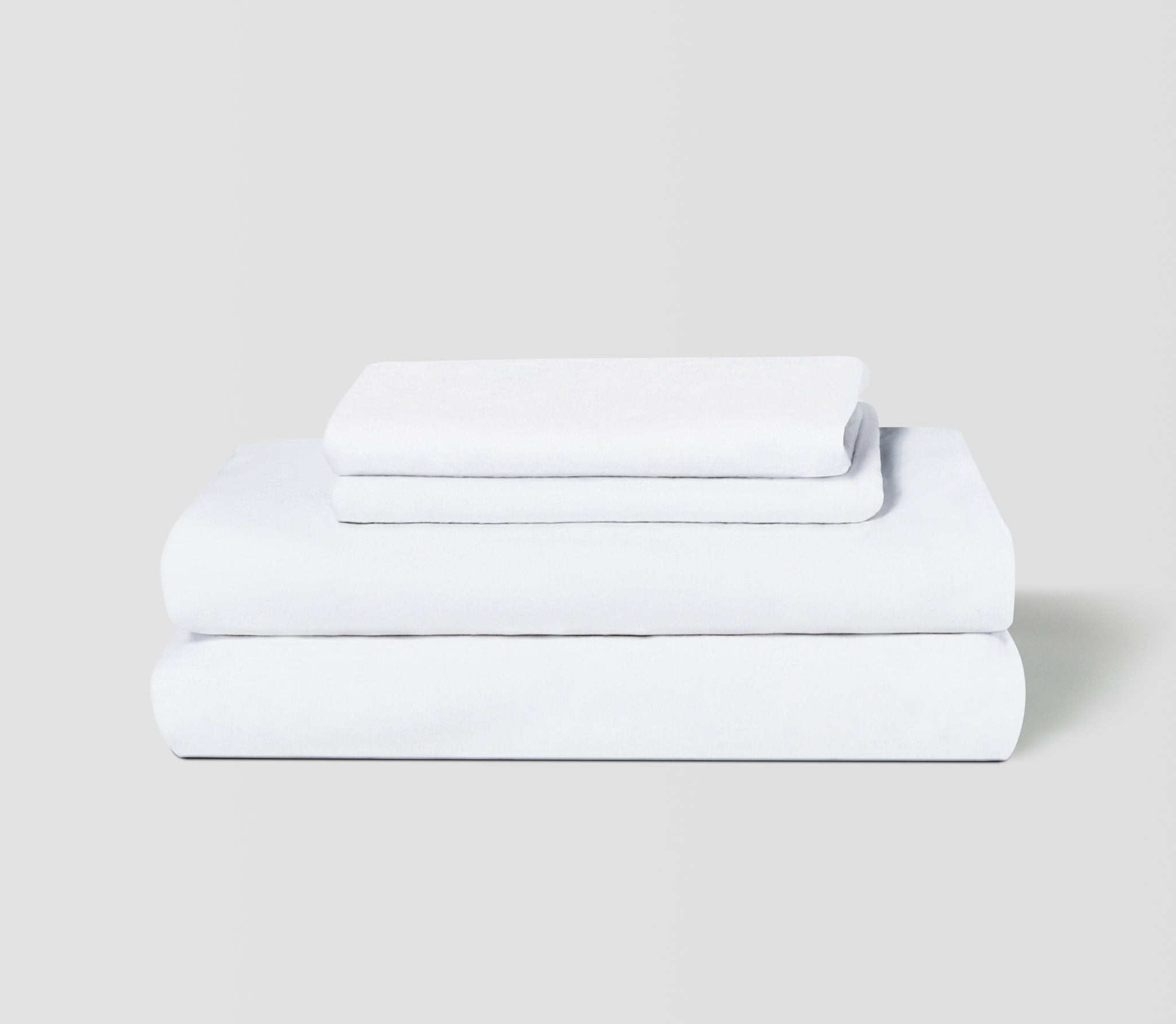 Folded set of two Essential White Linen Pillow Cases on top of a folded Linen Fitted Sheet and Flat Sheet.