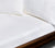 Wooden bed with close up of two Essential White Linen Pillows and Sheets.