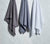Charcoal Grey, Slate Blue and Essential White Honeycomb Bath Towels hanging in a white marble bathroom.