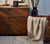 Wooden chest with decorative items on it, vase with feathers and basket with Natural Checked Throw hanging out.