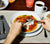 Person eating from a Dinner Bowl and Plate, a Mug of coffee and Classic Stainless Flatware also freatured.