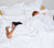 Woman and man sleeping in all white Percale bed. Woman and man have covers pulled up high.